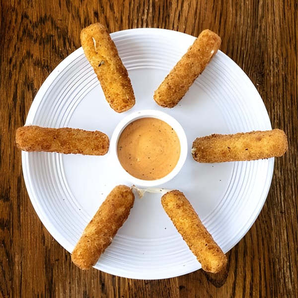 Six golden-brown mozzarella sticks arranged around a small bowl of dipping sauce on a white plate.