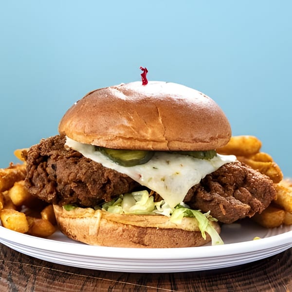 Holy Bowly's fried chicken sandwich with melted cheese, pickles, and lettuce, served with fries.