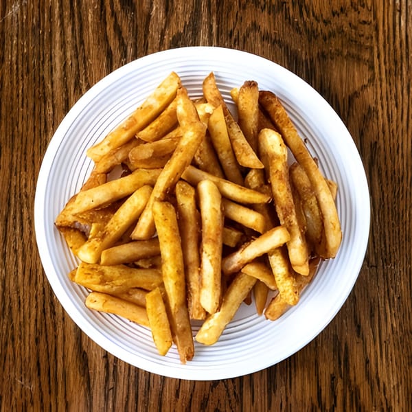 A white plate filled with golden-brown french fries, resting on a rustic wooden table.
