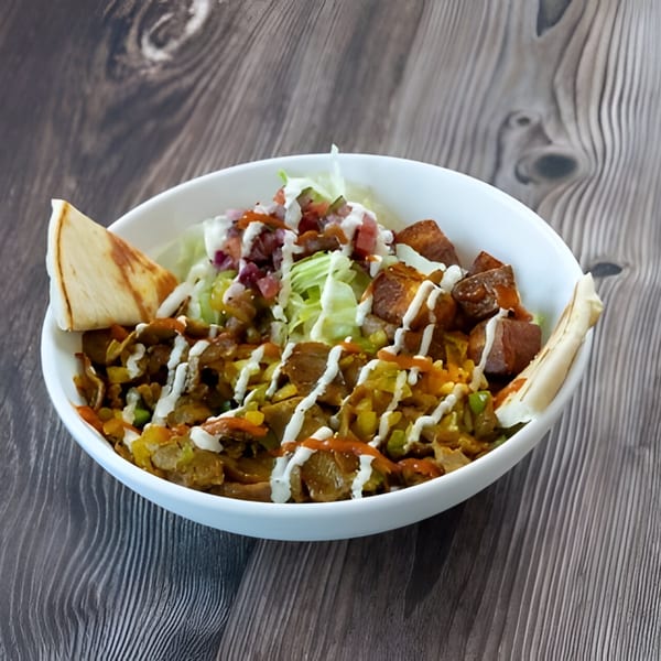 A Holy Bowly middle-eastern bowl with meat, vegetables, sauce, and pita bread on a wooden table.