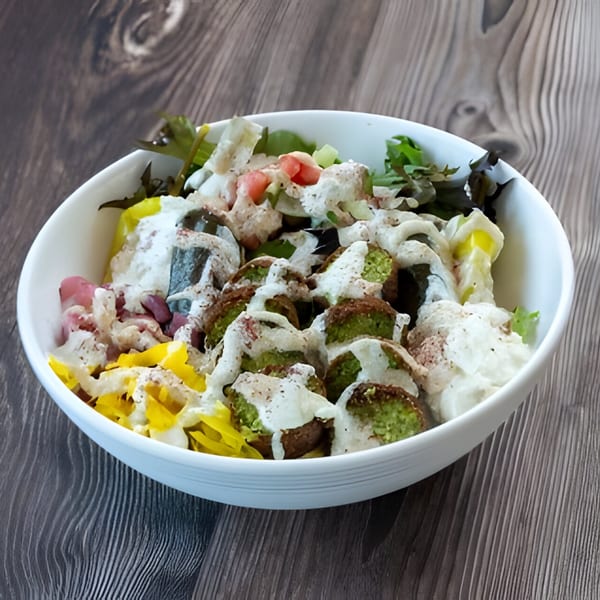 A Holy Bowly falafel bowl with tahini sauce, pickled vegetables, and greens on a wooden table.