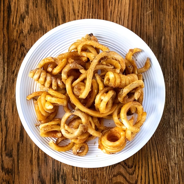 A white plate filled with golden-brown curly fries, set on a rustic wooden table.